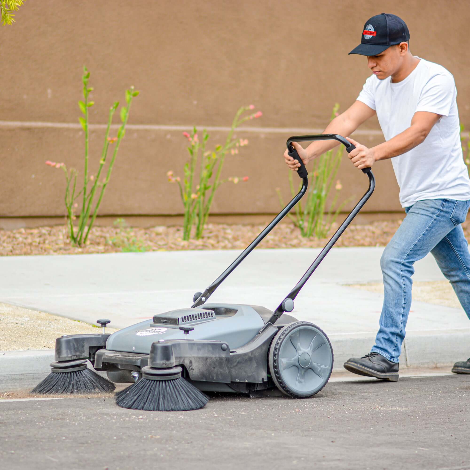 Pushing Tomahawk sweeper on sidewalk outside