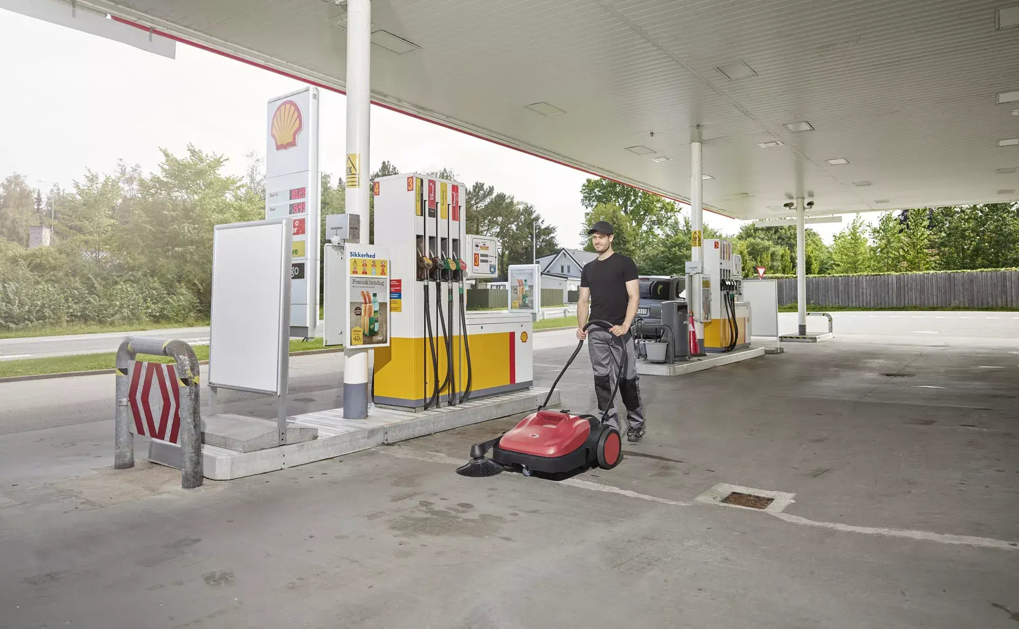 The Viper Manual Push sweeper in use outside at a gas station. 